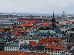 A panoramic view of Copenhagen's rooftops with iconic architecture and a distant harbor.