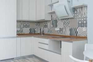 Interior of contemporary kitchen with white cabinets and wooden counter near ornamental tile on wall and modern appliances in apartment
