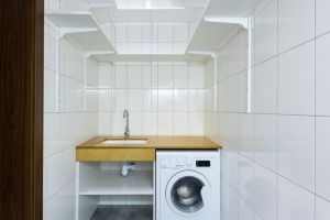 Modern laundry area with white tiled walls, washing machine, and built-in shelves.