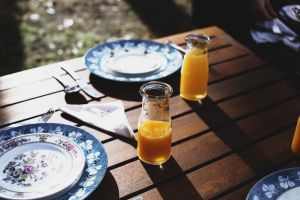 High angle of plates and forks with knifes near spoon and glass bottle with drink near napkin on wooden table in daylight in nature