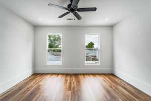 Modern minimalist bedroom featuring a ceiling fan and natural light from two windows in New Orleans.