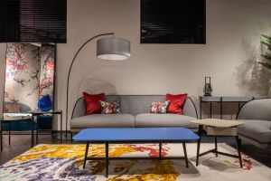 Comfortable sofa with colorful cushions placed at wall near armchair and table on carpet in spacious living room with lamp