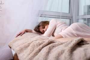 Woman in sleepwear resting in a cozy bedroom with soft light and warm tones.