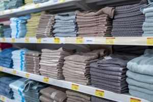 Neatly folded towels in various colors stacked on retail shelves inside a store.