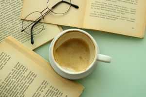 An inviting scene with a cup of coffee, open books, and eyeglasses for a cozy reading session.