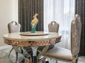 Statuette on round shaped table between classic chairs on marble floor in modern flat with curtains
