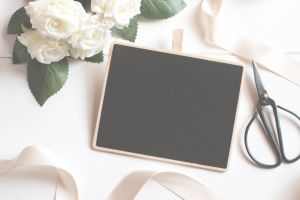 Chic flat lay of white roses, blank chalkboard, and scissors, perfect for creative projects.