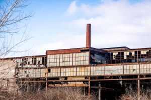 Exterior view of a decaying industrial factory with rusty steel and broken windows.