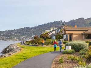Charming coastal residential area with people walking along a scenic pathway on a clear day.