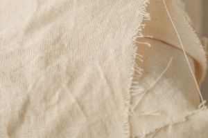 Detailed close-up of beige fabric showcasing frayed edges and texture, ideal for design and textile references.