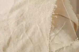 Detailed close-up of beige fabric showcasing frayed edges and texture, ideal for design and textile references.