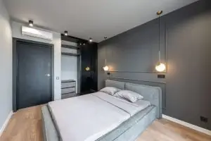 Contemporary minimalist style interior design of bedroom with comfortable bed placed near gray wall and with hanging and ceiling LED lamps