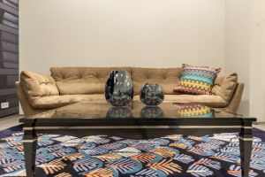 Comfortable couch with cushion and shining table with glowing decorations located on multicolored carpet in living room with yellow walls