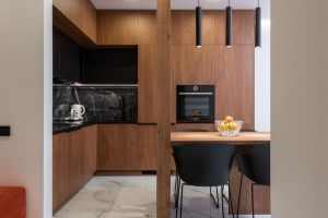 Modern kitchen interior with wooden furniture and dining table with vase of fresh fruits in stylish apartment