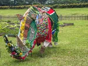 Vibrant rhinoceros sculpture made from recycled materials in a garden setting.
