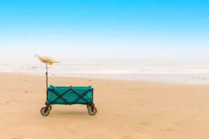 A folding wagon with a beach hat on a sunny sandy beach, perfect for a coastal adventure.