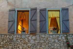 Evening view of a stone facade with illuminated windows and rustic shutters.