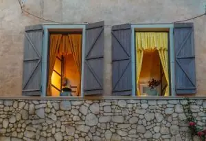 Evening view of a stone facade with illuminated windows and rustic shutters.